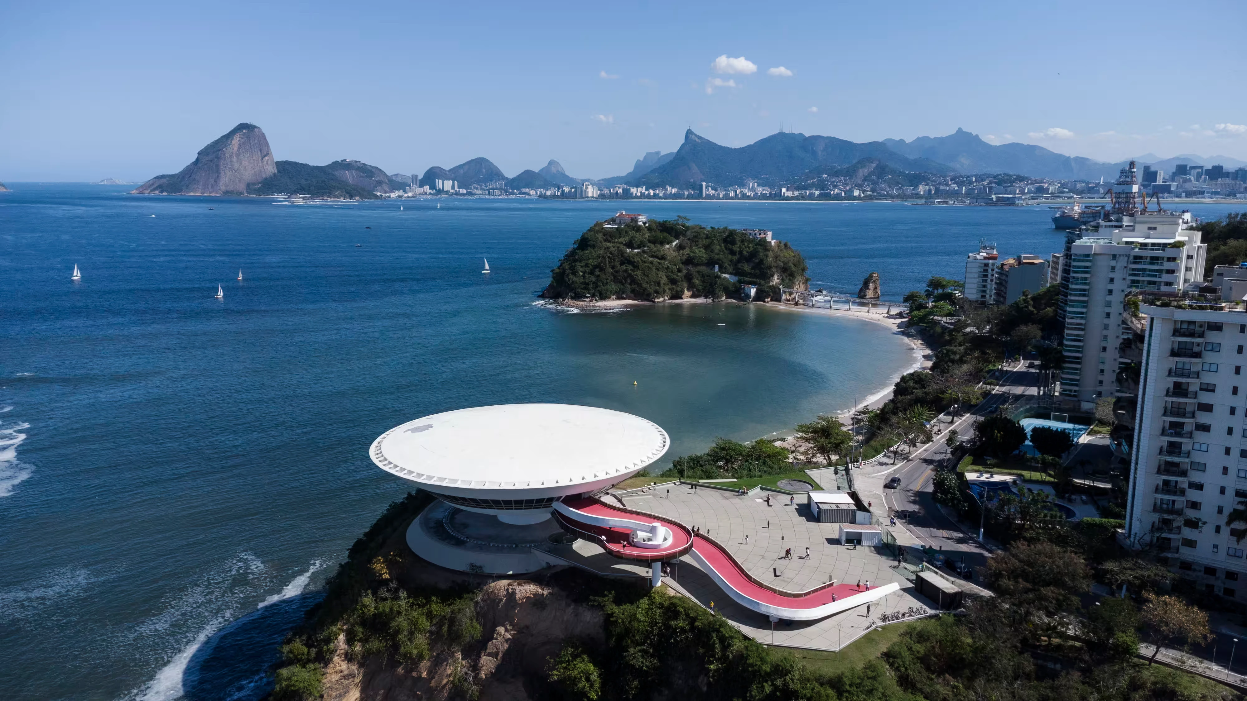 Foto de drone da vista superior do Museu de Arte Contemporãnea (MAC), com a Baía de Guanabara e Praia da Boa Viagem ao fundo.